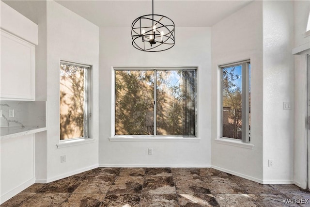 unfurnished dining area featuring baseboards, a chandelier, and a wealth of natural light