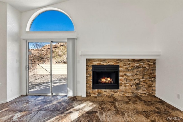 unfurnished living room with stone finish flooring, a tiled fireplace, and baseboards