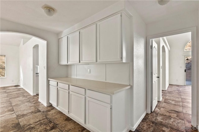 hall featuring stone finish floor, baseboards, and arched walkways