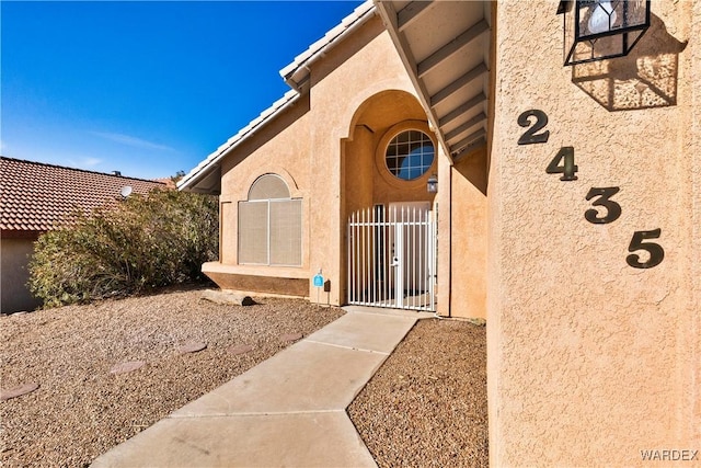 doorway to property with a tiled roof, a gate, and stucco siding