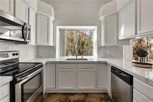 kitchen with stainless steel appliances, white cabinetry, a sink, and backsplash