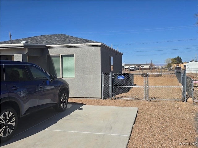 view of side of home with stucco siding, a shingled roof, fence, and a gate