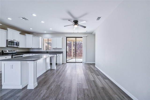 6102 S Scorpion Ln, Fort Mohave, AZ 86426 - kitchen with appliances with stainless steel finishes, dark countertops, dark wood-type flooring, white cabinetry, and a center island