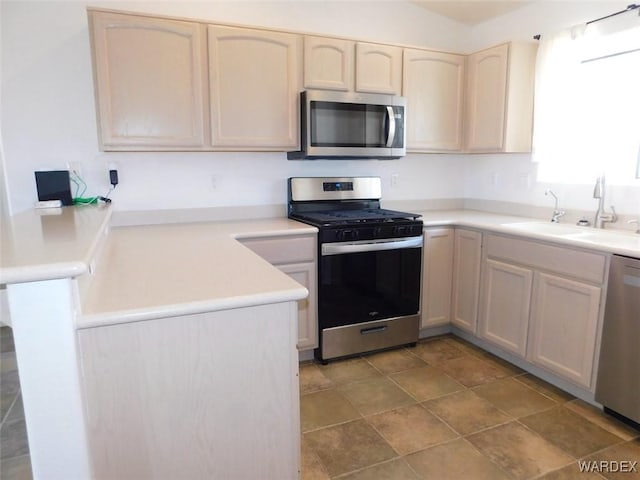 kitchen featuring a peninsula, appliances with stainless steel finishes, light countertops, and a sink