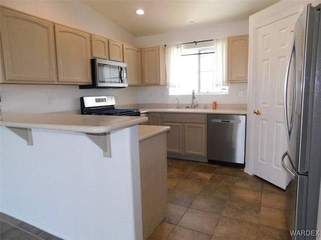 kitchen featuring a breakfast bar area, a peninsula, stainless steel appliances, light countertops, and a sink