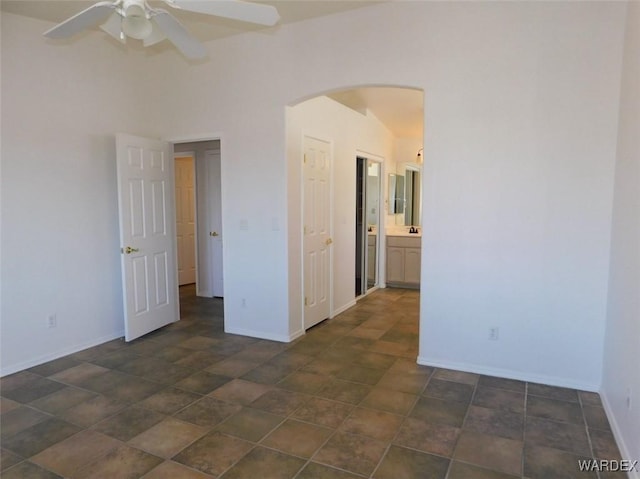 empty room featuring arched walkways, ceiling fan, and baseboards