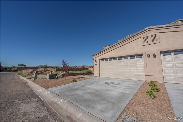 view of side of property featuring a garage, concrete driveway, and stucco siding