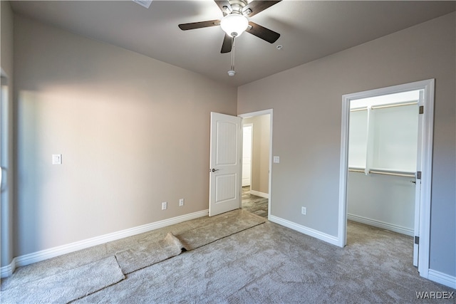 unfurnished bedroom with a ceiling fan, light carpet, a spacious closet, and baseboards