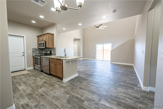 kitchen with a peninsula, a sink, open floor plan, appliances with stainless steel finishes, and brown cabinets