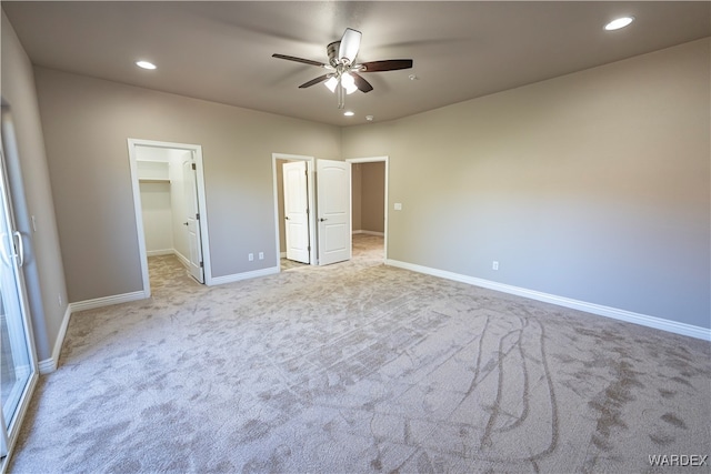 unfurnished bedroom featuring a walk in closet, recessed lighting, light colored carpet, a ceiling fan, and baseboards