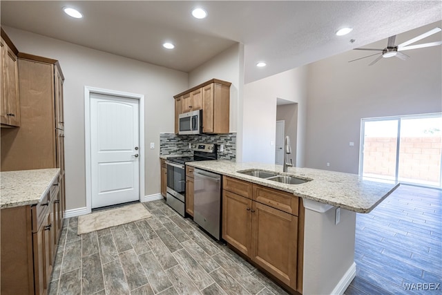 kitchen with stainless steel appliances, wood finished floors, a sink, brown cabinets, and decorative backsplash