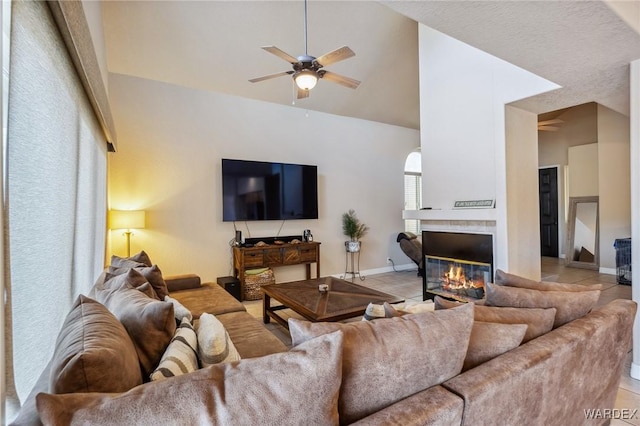 living room featuring light tile patterned floors, lofted ceiling, a ceiling fan, a glass covered fireplace, and baseboards