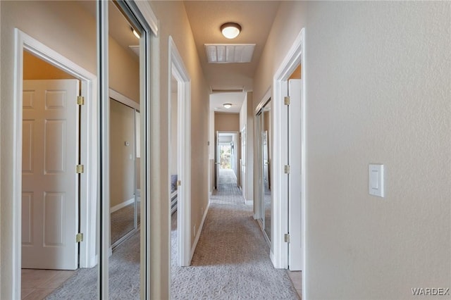 hall with light carpet, light tile patterned floors, and visible vents