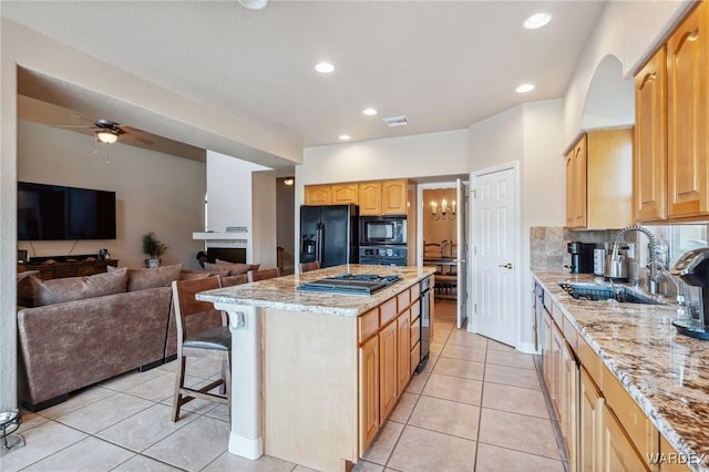 kitchen with open floor plan, a kitchen island, a sink, light stone countertops, and black appliances