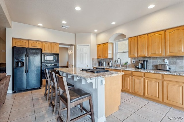 kitchen with light stone counters, a center island, visible vents, a sink, and black appliances