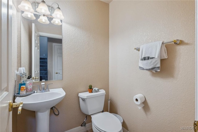 half bath with a textured wall, a notable chandelier, and toilet