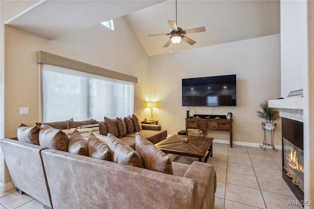 living room with baseboards, a ceiling fan, a glass covered fireplace, lofted ceiling, and light tile patterned flooring