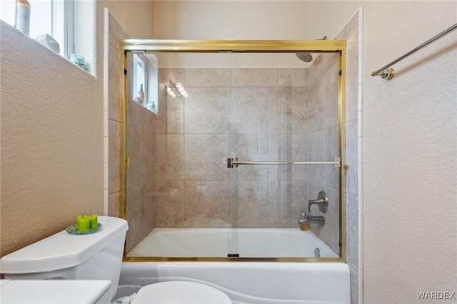 bathroom with enclosed tub / shower combo, a textured wall, and toilet