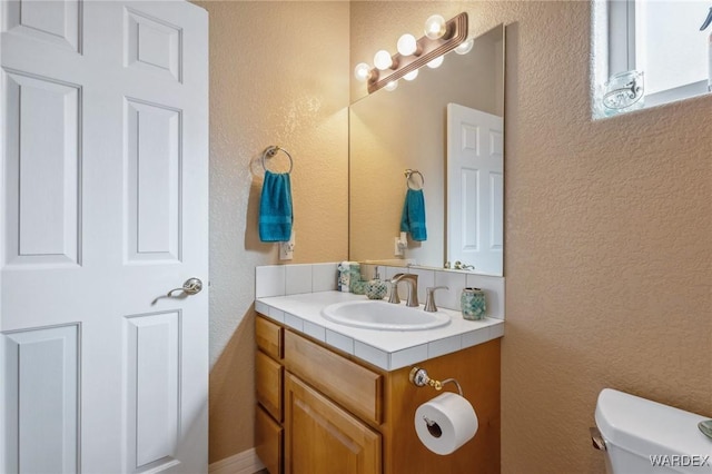 half bath with toilet, a textured wall, and vanity