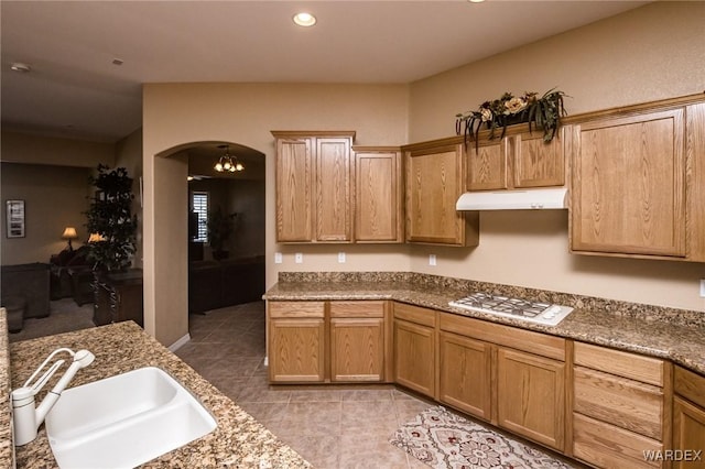 kitchen with light tile patterned floors, white gas stovetop, arched walkways, under cabinet range hood, and a sink