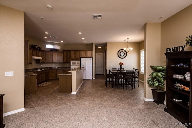 kitchen with white appliances, visible vents, a kitchen island, light stone counters, and decorative light fixtures