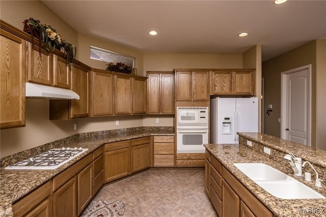 kitchen featuring brown cabinets, recessed lighting, a sink, white appliances, and under cabinet range hood