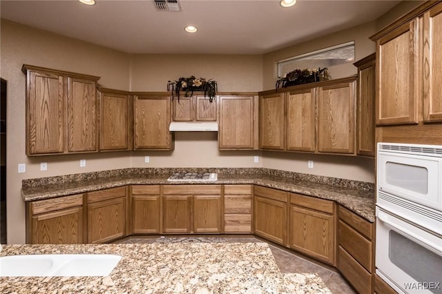 kitchen with white appliances, under cabinet range hood, visible vents, and brown cabinetry