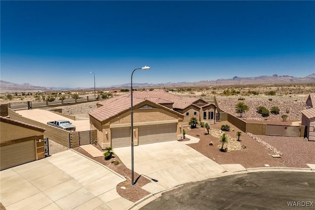 view of front facade with a mountain view, fence, concrete driveway, a gate, and stucco siding