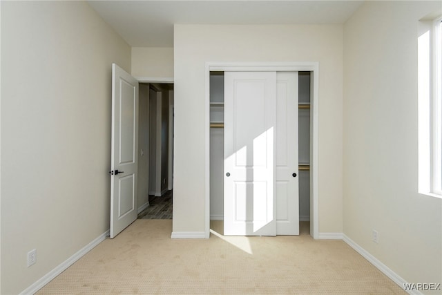 unfurnished bedroom with baseboards, a closet, and light colored carpet