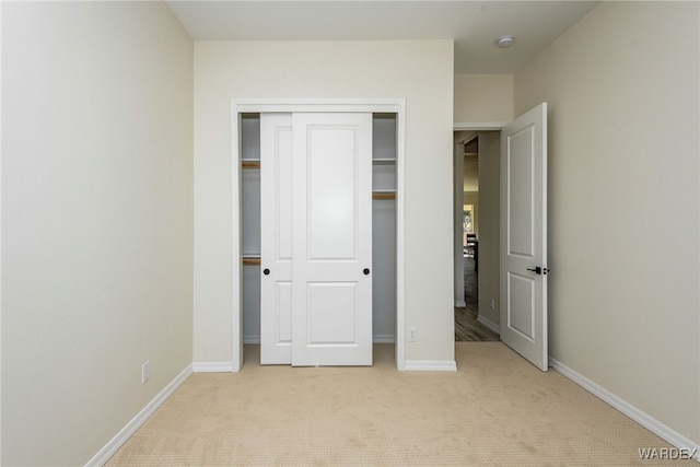 unfurnished bedroom with a closet, light carpet, and baseboards