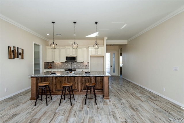 kitchen featuring stainless steel microwave, hanging light fixtures, a large island, and light stone countertops