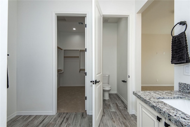 bathroom featuring toilet, wood finished floors, vanity, baseboards, and a spacious closet