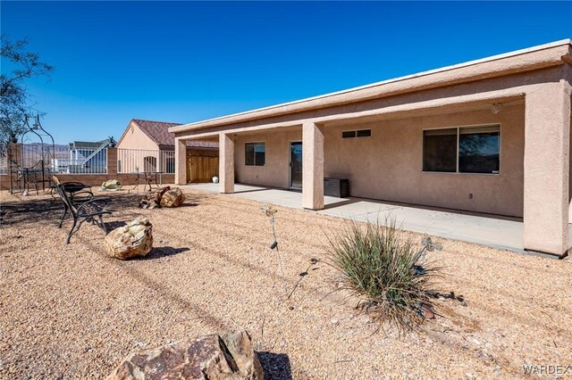 rear view of property featuring a patio area, fence, and stucco siding