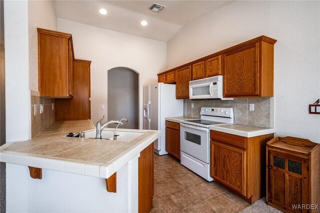 kitchen featuring a peninsula, white appliances, a sink, visible vents, and a kitchen breakfast bar