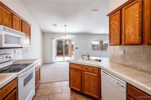 kitchen featuring tile counters, visible vents, decorative backsplash, a sink, and white appliances