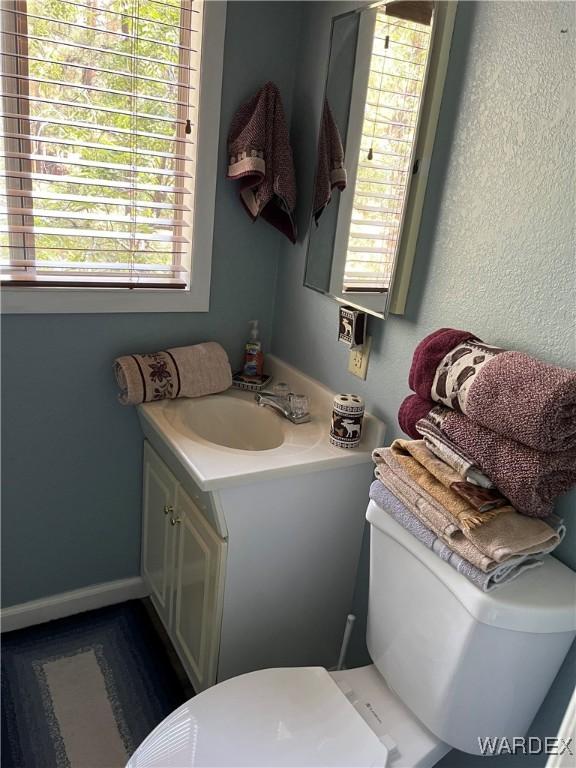 half bath with toilet, baseboards, and vanity