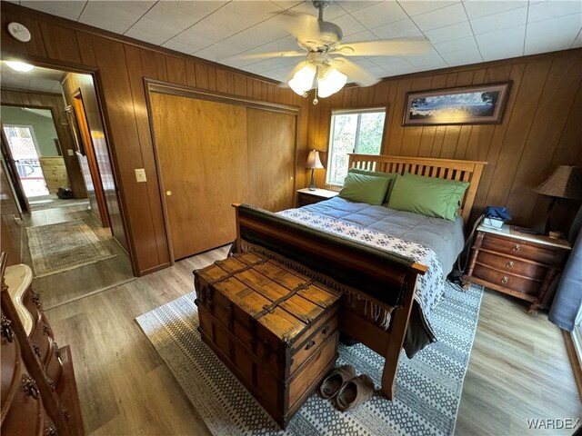 bedroom featuring ceiling fan, wood walls, a closet, and light wood-style flooring