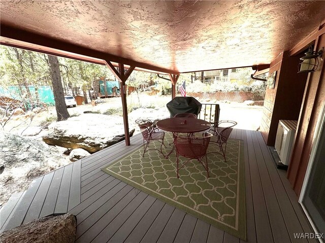 snow covered deck with outdoor dining space, fence, and a grill