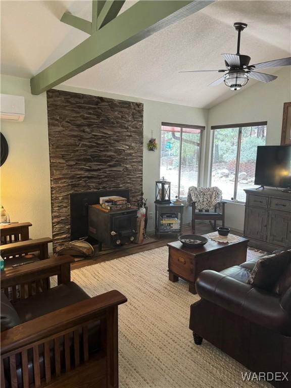 living room with vaulted ceiling with beams, an AC wall unit, a wood stove, ceiling fan, and a textured ceiling