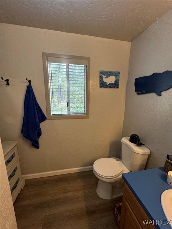 half bathroom with toilet, a textured ceiling, wood finished floors, and vanity