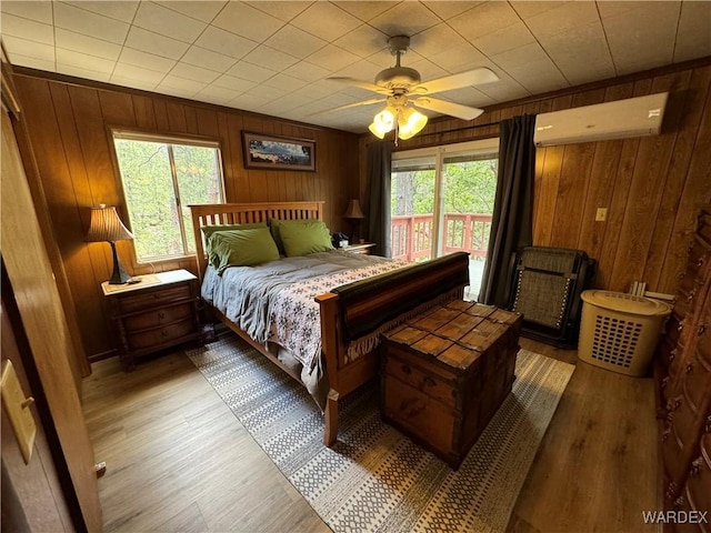 bedroom featuring access to exterior, an AC wall unit, wood finished floors, and wooden walls