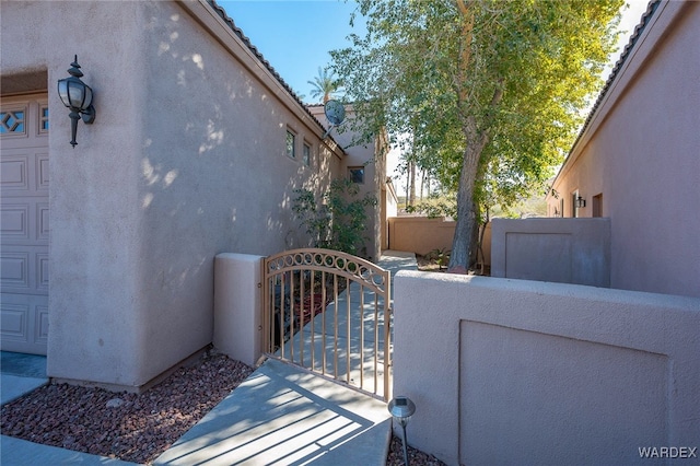 view of side of property with a tiled roof, fence, a gate, and stucco siding