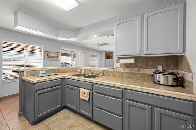 kitchen featuring a peninsula, decorative backsplash, gray cabinets, and a sink