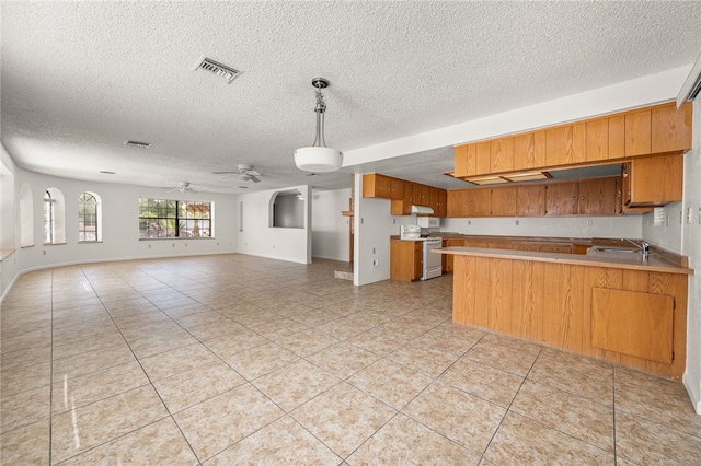 2218 Family Cir, Bullhead City, AZ 86442 - kitchen with white range oven, brown cabinetry, a textured ceiling, a peninsula, and light tile patterned floors