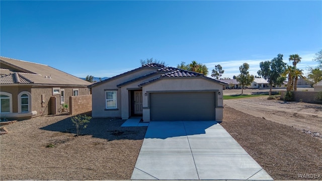 view of front facade featuring a garage, concrete driveway, a tile roof, fence, and stucco siding