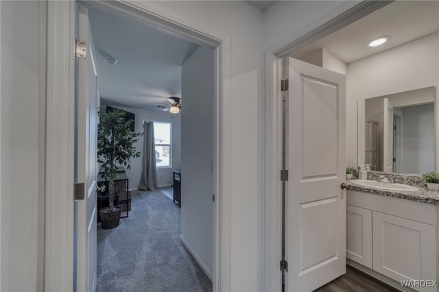 hall featuring baseboards, dark carpet, and a sink