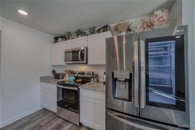 kitchen featuring baseboards, light stone counters, stainless steel appliances, light wood-type flooring, and white cabinetry