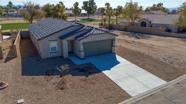 view of front facade with a tile roof, stucco siding, concrete driveway, an attached garage, and fence