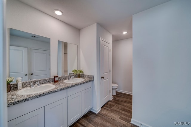 bathroom with double vanity, a sink, toilet, and wood finished floors