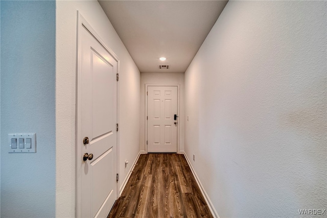 hallway with baseboards, visible vents, and dark wood finished floors